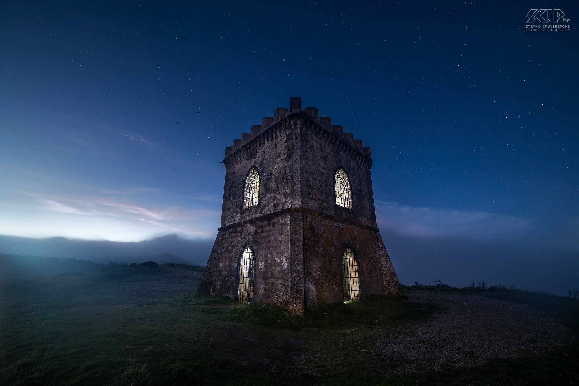 Castelo Branco by night The tower of the Castelo Branco at the end of the blue hour with some fog at the high hilltop. The Miradouro do Castelo Branco is a viewpoint at the main island São Miguel of the Azores. From there you can see the village of Villa Franca do Compo, the Furnas Lake and the Atlantic Ocean. The tower looks like a medieval fortress but it is more recent and constructed with concrete. I used some flash lights to illuminate  the insides of the tower. Stefan Cruysberghs